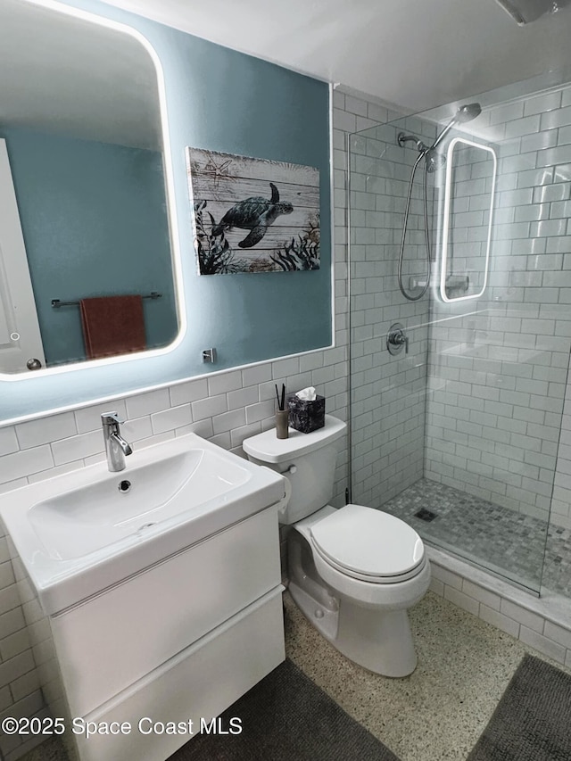 bathroom with tile walls, vanity, toilet, and tiled shower