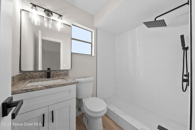 bathroom featuring hardwood / wood-style floors, vanity, a tile shower, a textured ceiling, and toilet