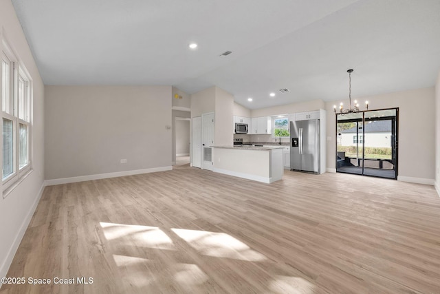 unfurnished living room featuring vaulted ceiling, an inviting chandelier, and light hardwood / wood-style floors