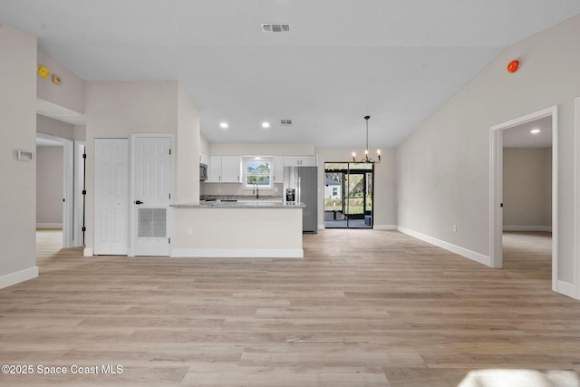 unfurnished living room featuring lofted ceiling, sink, light hardwood / wood-style floors, and a chandelier