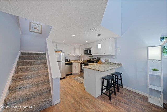 8600 Ridgewood Ave Unit 1308, Cape Canaveral, FL 32920 - kitchen featuring appliances with stainless steel finishes, a peninsula, light wood-style flooring, white cabinets, and a textured ceiling