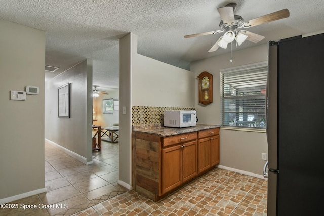 kitchen with ceiling fan, stainless steel fridge, light stone countertops, and a textured ceiling