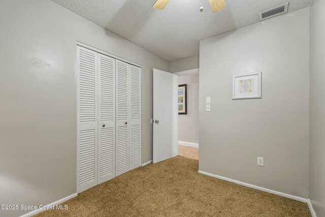 unfurnished bedroom with ceiling fan, light carpet, a closet, and a textured ceiling