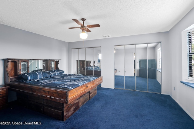 bedroom featuring multiple closets, dark colored carpet, a textured ceiling, and ceiling fan