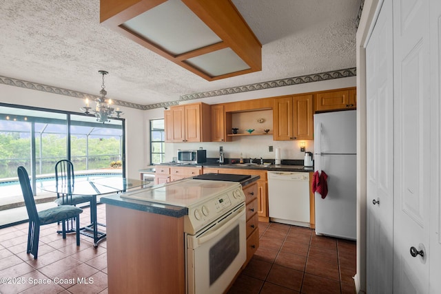 kitchen featuring decorative light fixtures, sink, dark tile patterned floors, a center island, and white appliances