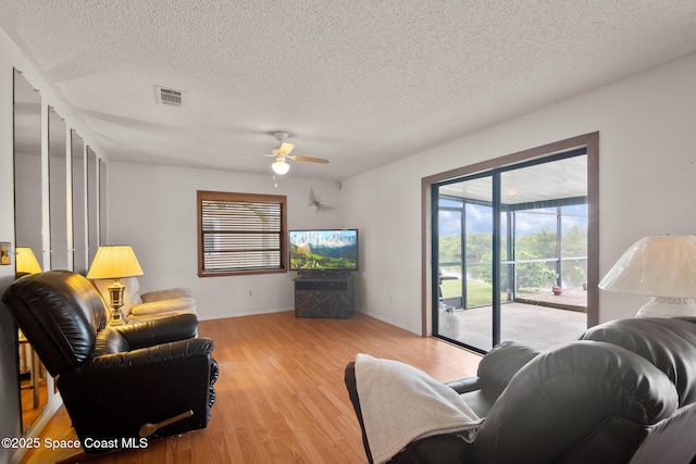 living room featuring ceiling fan, a textured ceiling, and light wood-type flooring