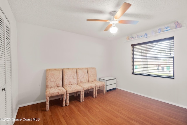 living area featuring wood-type flooring, ceiling fan, and a textured ceiling