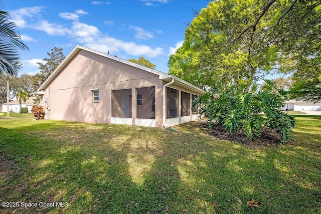 rear view of property with a yard, a sunroom, and stucco siding