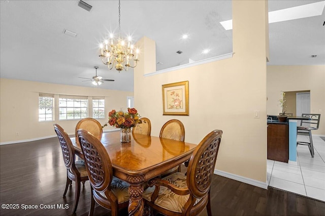 dining area with ceiling fan with notable chandelier, baseboards, wood finished floors, a towering ceiling, and visible vents