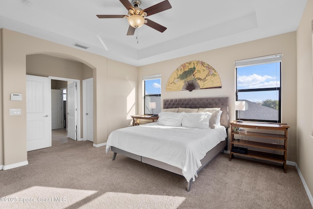 bedroom featuring baseboards, visible vents, a raised ceiling, arched walkways, and light colored carpet