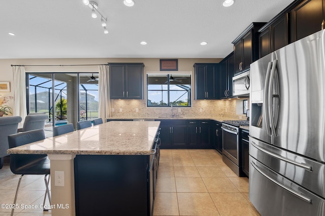 kitchen featuring light tile patterned floors, a ceiling fan, a breakfast bar area, a center island, and stainless steel appliances