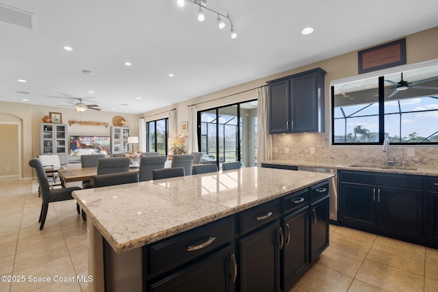 kitchen featuring arched walkways, light stone counters, a sink, and a center island