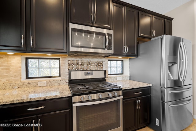 kitchen with light stone countertops, dark brown cabinetry, stainless steel appliances, and backsplash