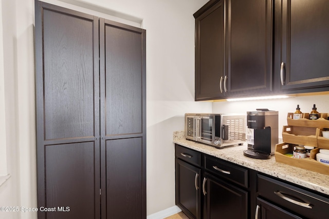 kitchen featuring light stone counters and dark brown cabinetry