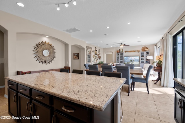 kitchen featuring arched walkways, light stone counters, light tile patterned flooring, a kitchen island, and open floor plan