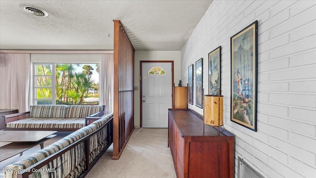 doorway to outside with a textured ceiling, brick wall, visible vents, and light colored carpet