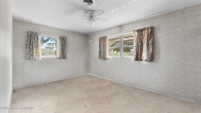 carpeted empty room with a textured ceiling, a textured wall, plenty of natural light, and visible vents