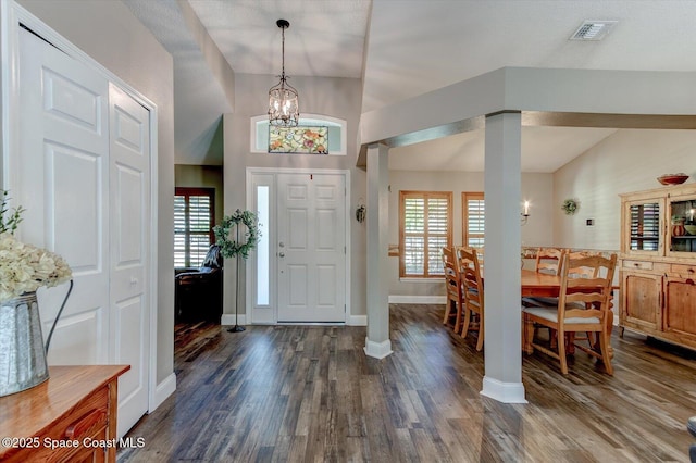 foyer entrance with decorative columns, dark wood-type flooring, lofted ceiling, and a notable chandelier