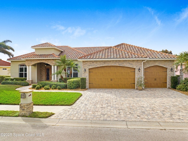 mediterranean / spanish house with an attached garage, stone siding, a tile roof, and decorative driveway