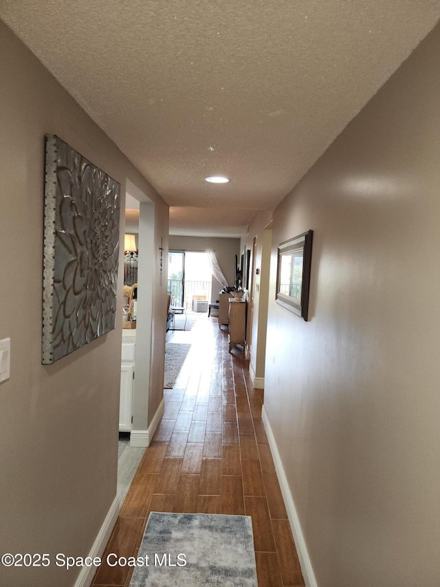 hall with a textured ceiling, baseboards, and wood tiled floor