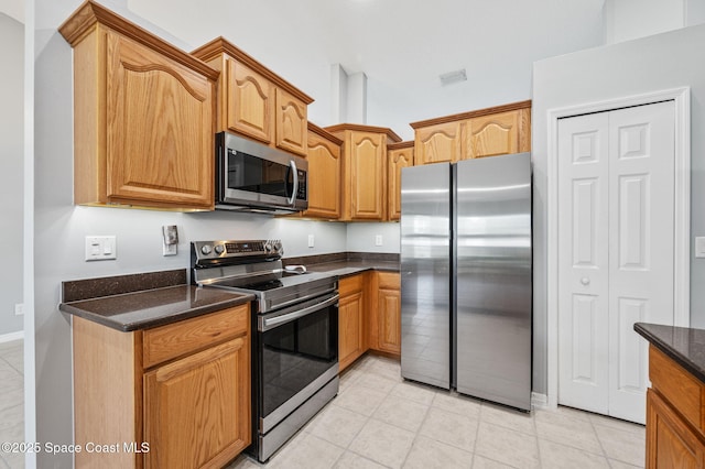 kitchen featuring dark stone counters, appliances with stainless steel finishes, light tile patterned flooring, and visible vents