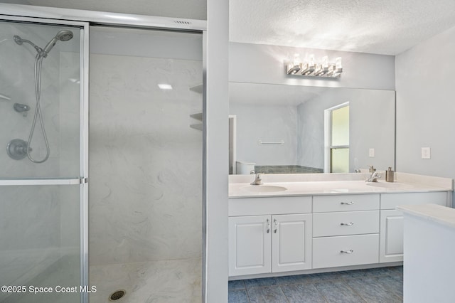 bathroom with double vanity, a shower stall, and a textured ceiling