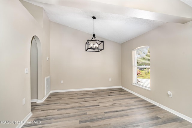 empty room featuring wood-type flooring, lofted ceiling, a notable chandelier, and a textured ceiling