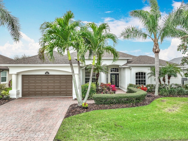 view of front of home featuring decorative driveway, an attached garage, a front yard, and stucco siding