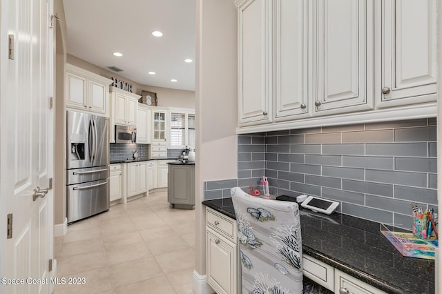 kitchen with light tile patterned flooring, dark stone countertops, stainless steel appliances, decorative backsplash, and white cabinets