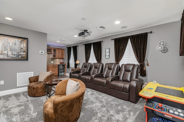 carpeted home theater room featuring indoor bar, beverage cooler, and a textured ceiling