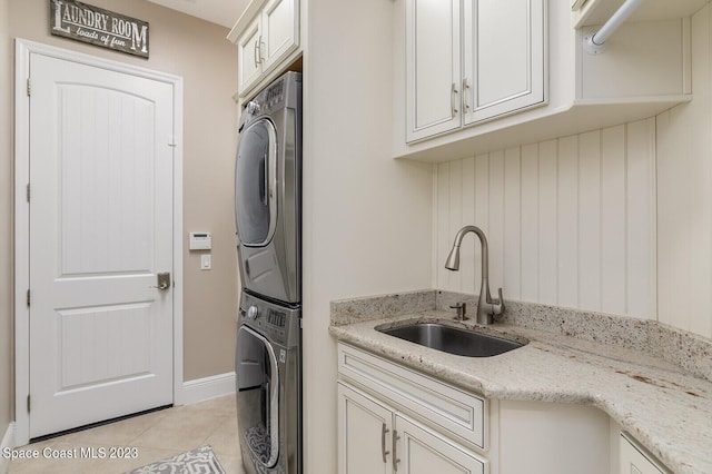 washroom featuring sink, light tile patterned floors, cabinets, and stacked washer and clothes dryer