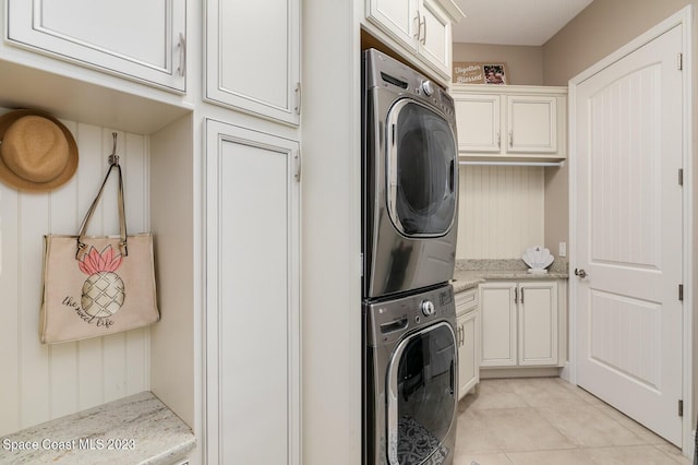 clothes washing area featuring cabinets, stacked washer and dryer, and light tile patterned floors