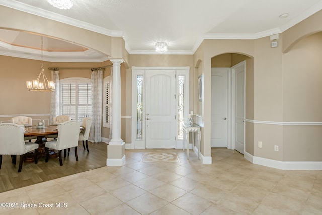 tiled entryway with decorative columns, crown molding, a chandelier, and a tray ceiling