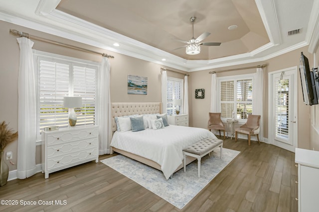 bedroom featuring access to exterior, crown molding, wood-type flooring, and a raised ceiling