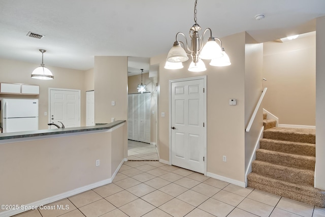 kitchen with light tile patterned flooring, sink, white refrigerator, hanging light fixtures, and an inviting chandelier