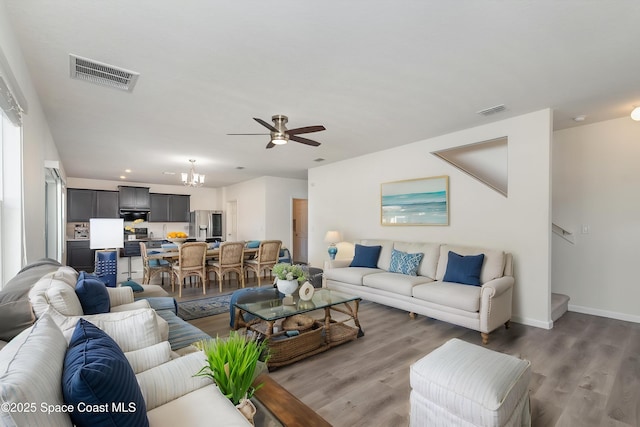 living room featuring visible vents, baseboards, ceiling fan with notable chandelier, and wood finished floors