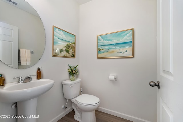 half bath with toilet, baseboards, visible vents, and wood finished floors