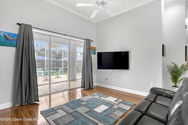 living room featuring a ceiling fan, crown molding, baseboards, and wood finished floors