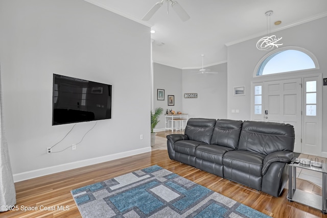 living room with ornamental molding, ceiling fan with notable chandelier, baseboards, and wood finished floors