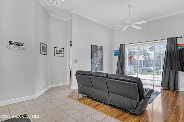 living room featuring baseboards, a ceiling fan, light wood-style flooring, a high ceiling, and crown molding