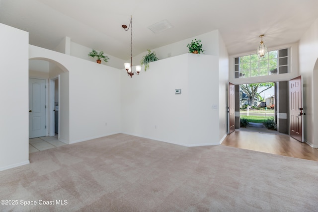 spare room with a notable chandelier, light colored carpet, and a high ceiling