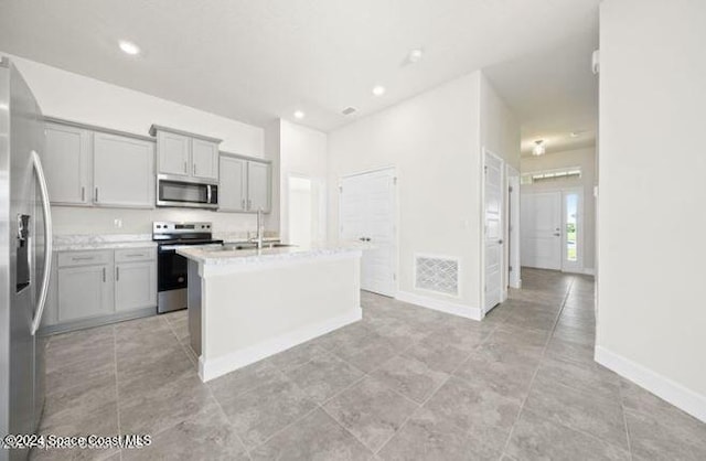 kitchen featuring light stone counters, stainless steel appliances, gray cabinets, and an island with sink