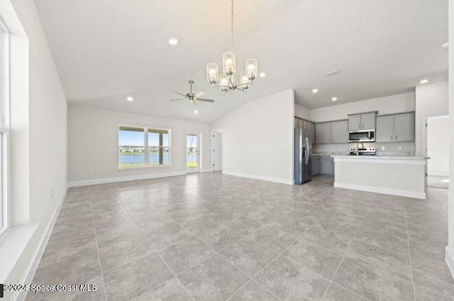 unfurnished living room featuring vaulted ceiling and ceiling fan with notable chandelier