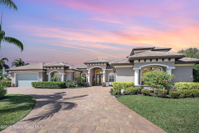 mediterranean / spanish-style house with a garage, a tile roof, decorative driveway, and stucco siding