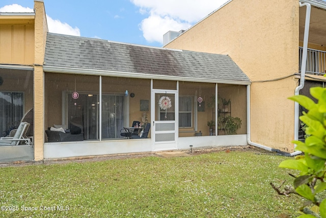 back of property featuring a sunroom, roof with shingles, a lawn, and stucco siding