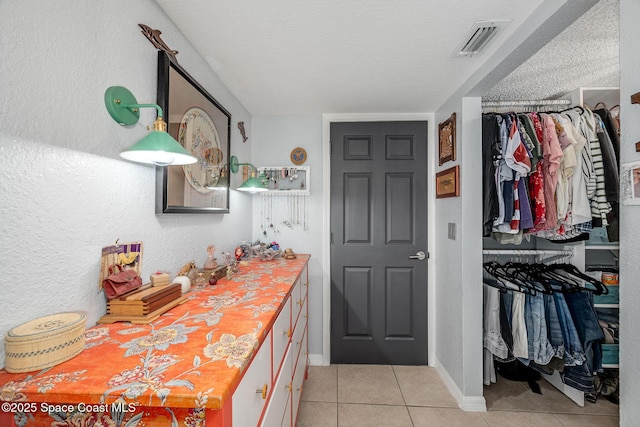 interior space with baseboards, visible vents, tile patterned floors, a walk in closet, and a textured ceiling