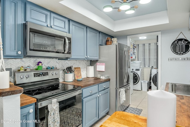 kitchen featuring blue cabinetry, butcher block countertops, washer and clothes dryer, and stainless steel appliances