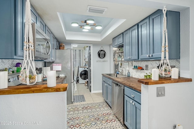 kitchen featuring butcher block counters, a sink, appliances with stainless steel finishes, a tray ceiling, and washer / dryer