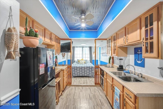 kitchen with sink, light hardwood / wood-style flooring, black refrigerator, a tray ceiling, and ceiling fan