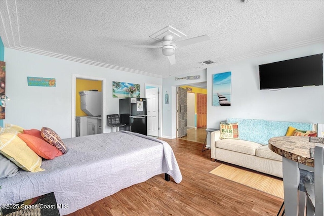 bedroom featuring black refrigerator, wood-type flooring, ornamental molding, ceiling fan, and a textured ceiling